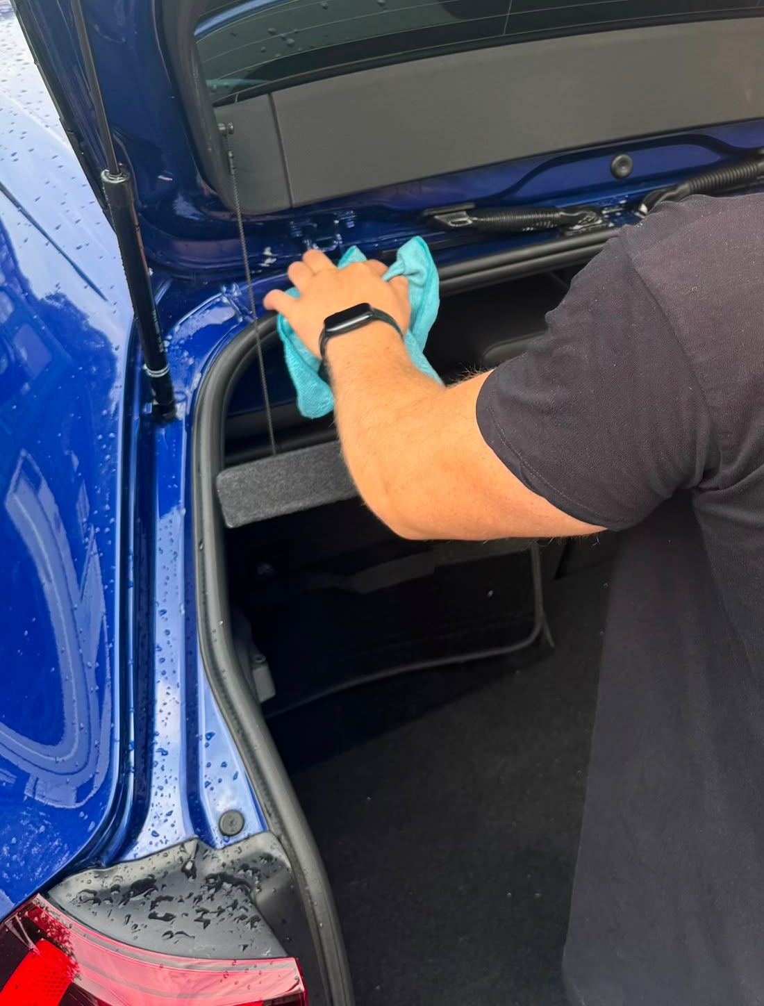 Hand mit Mikrofasertuch reinigt die Kofferraumkante eines blauen VW Golf R